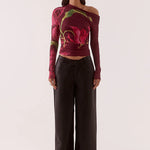 Woman wearing a colorful off-shoulder top with floral patterns and black pants on a white background