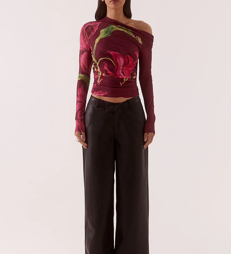 Woman wearing a colorful off-shoulder top with floral patterns and black pants on a white background