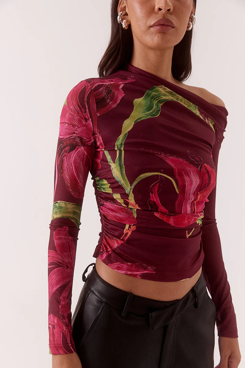 Woman wearing a colorful off-shoulder top with floral patterns and black pants on a white background