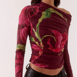 Woman wearing a colorful off-shoulder top with floral patterns and black pants on a white background