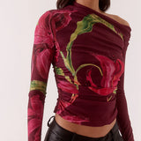Woman wearing a colorful off-shoulder top with floral patterns and black pants on a white background