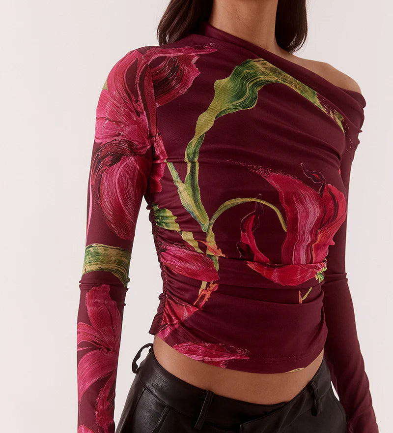 Woman wearing a colorful off-shoulder top with floral patterns and black pants on a white background