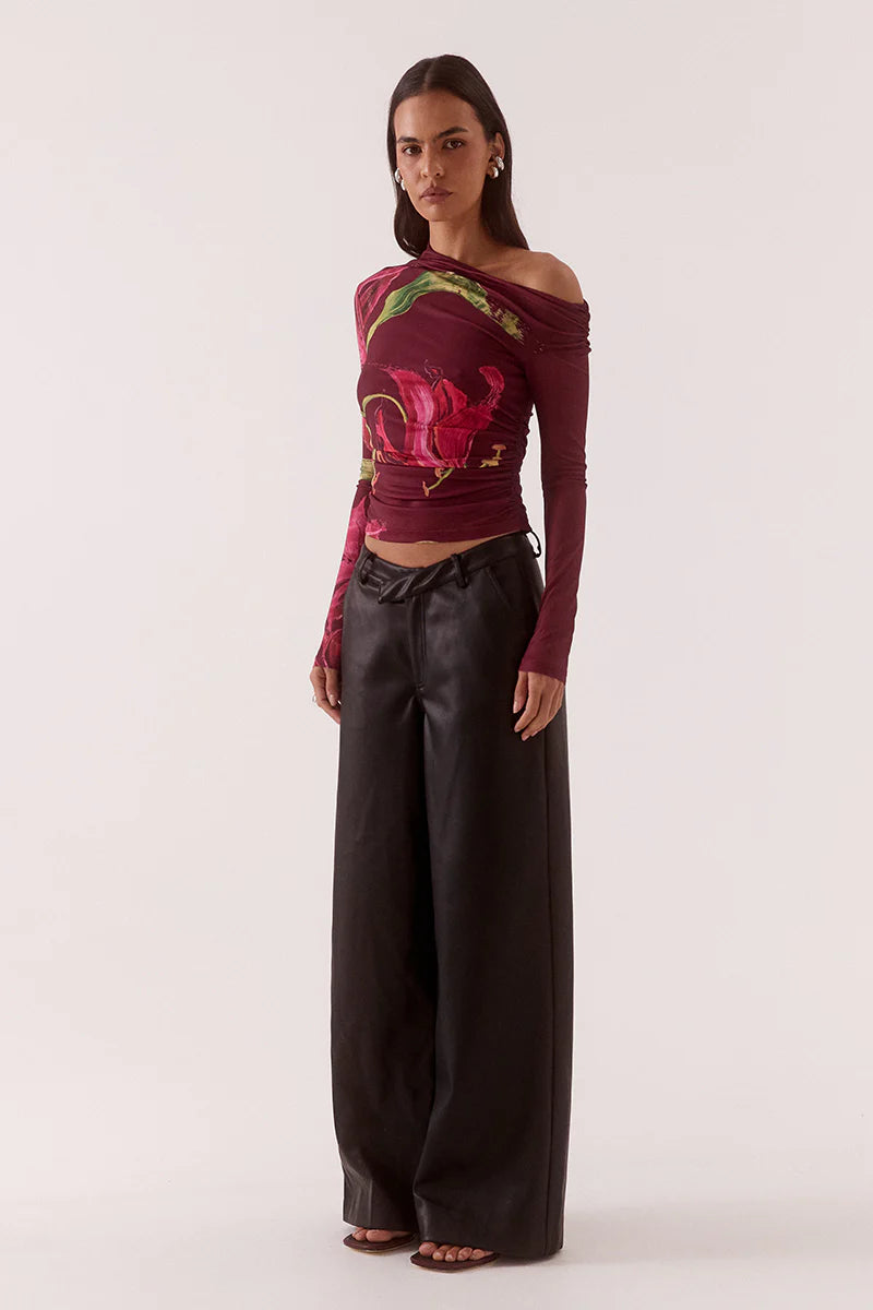 Woman wearing a colorful off-shoulder top with floral patterns and black pants on a white background