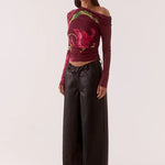 Woman wearing a colorful off-shoulder top with floral patterns and black pants on a white background