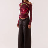 Woman wearing a colorful off-shoulder top with floral patterns and black pants on a white background