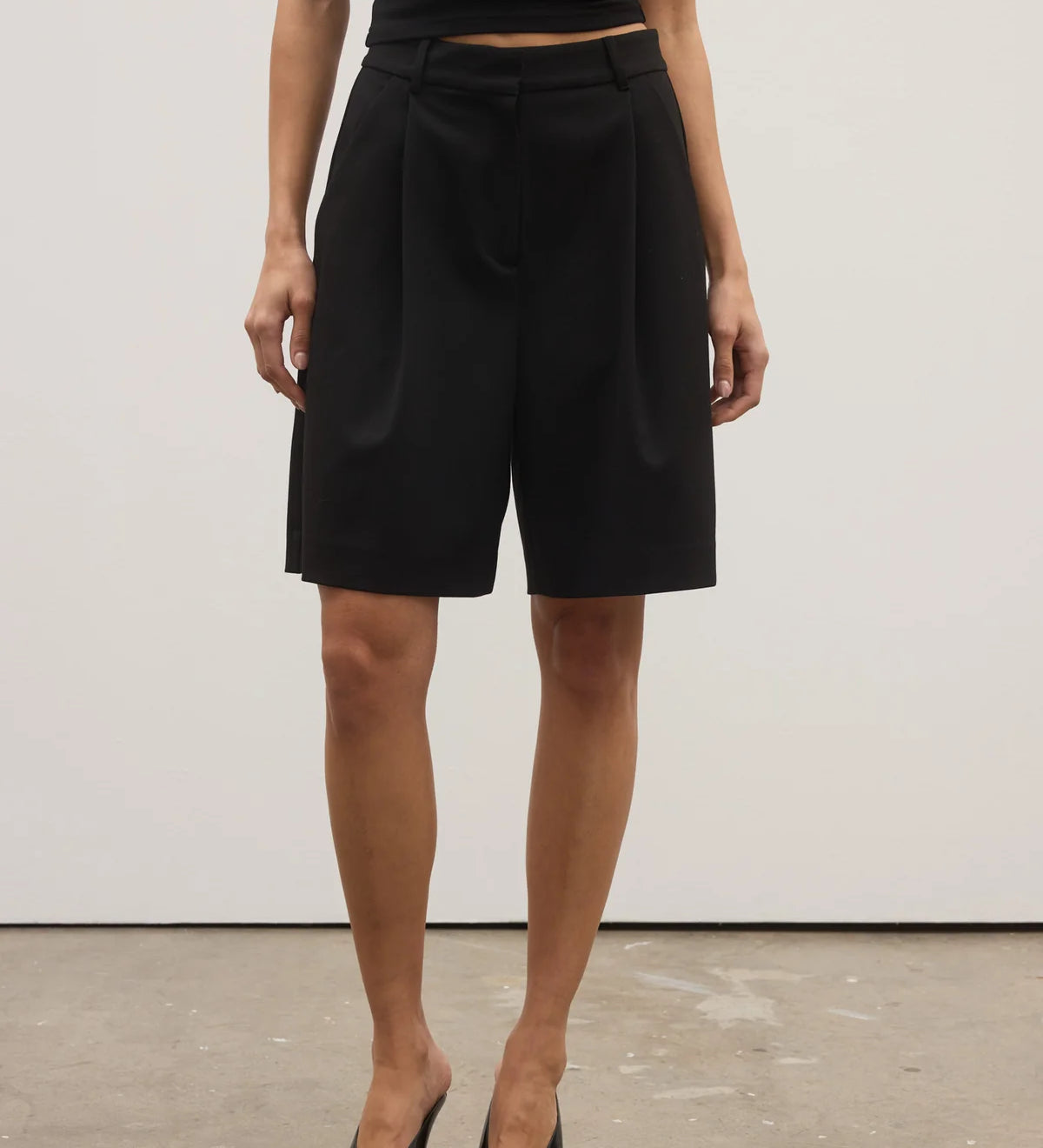 Person wearing black shorts and black shoes on a plain background