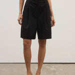 Person wearing black shorts and black shoes on a plain background