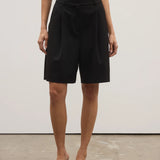 Person wearing black shorts and black shoes on a plain background