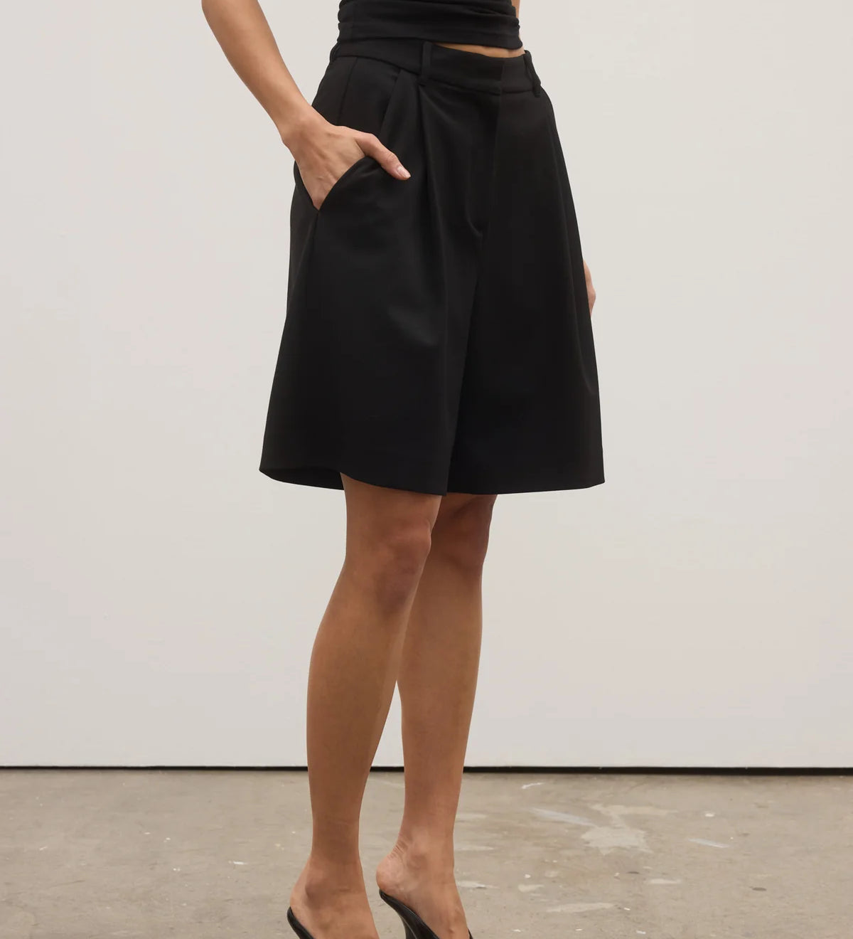 Person wearing a black skirt and black high-heeled shoes on a plain background