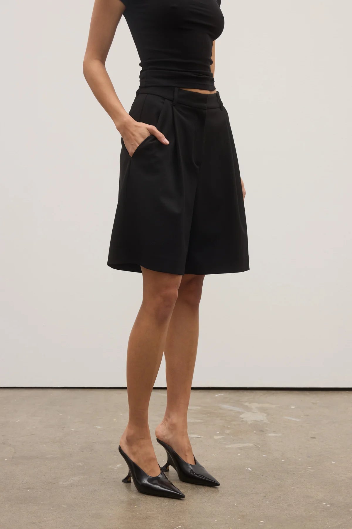Person wearing a black skirt and black high-heeled shoes on a plain background