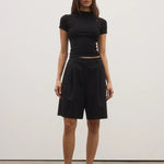 Woman wearing a black outfit standing against a white wall.