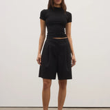 Woman wearing a black outfit standing against a white wall.