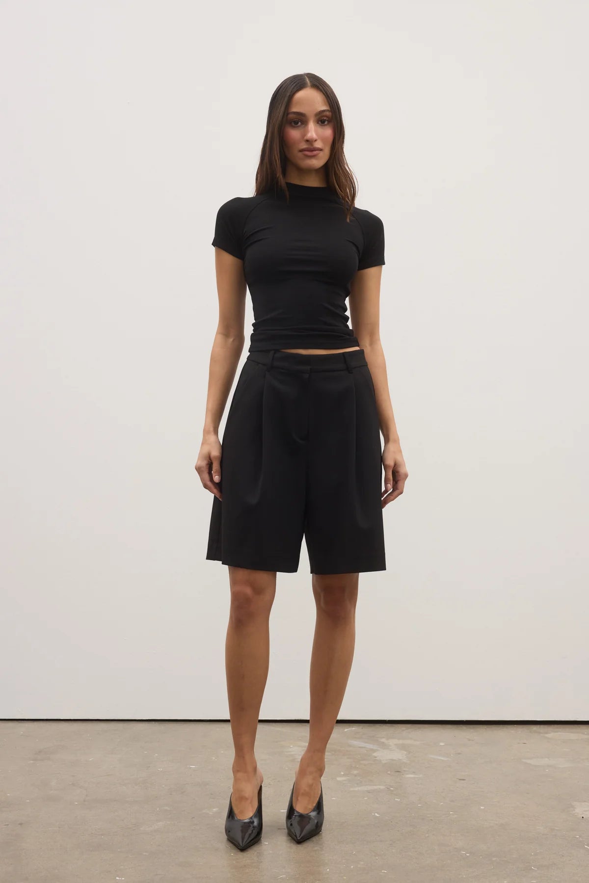 Woman wearing a black outfit standing against a white wall.