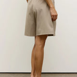 Person wearing beige shorts and white high-heeled shoes on a plain background