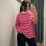 Person wearing a pink striped long sleeve  top taking a mirror selfie in a room with white walls and a gray curtain.