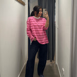 Person wearing a pink striped shirt and dark pants standing in a hallway.