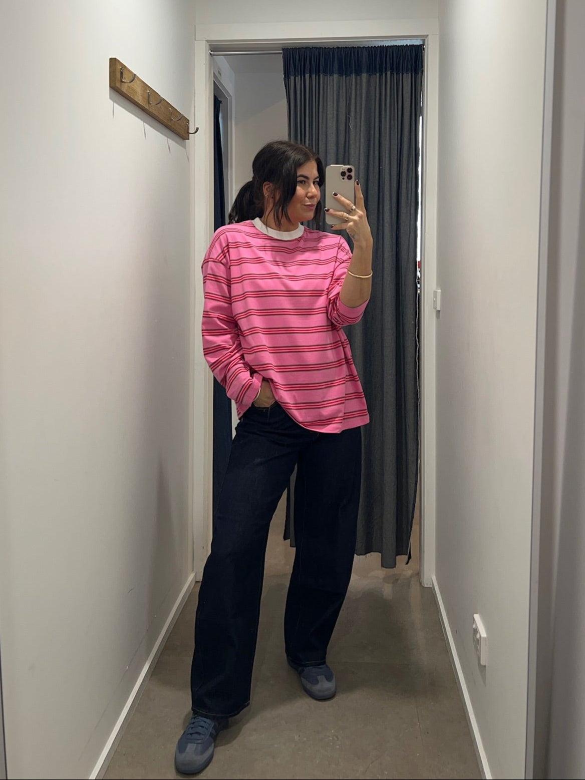 Person wearing a pink striped shirt and dark pants standing in a hallway.