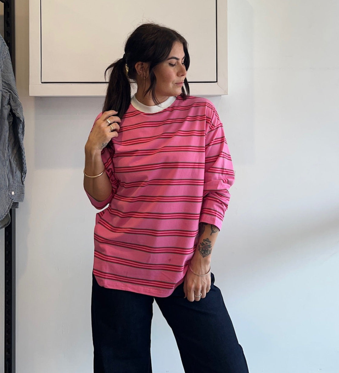 Person wearing a pink striped shirt standing in front of a white wall with a framed picture.
