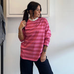 Person wearing a pink striped shirt standing in front of a white wall with a framed picture.