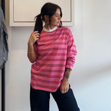 Person wearing a pink striped shirt standing in front of a white wall with a framed picture.
