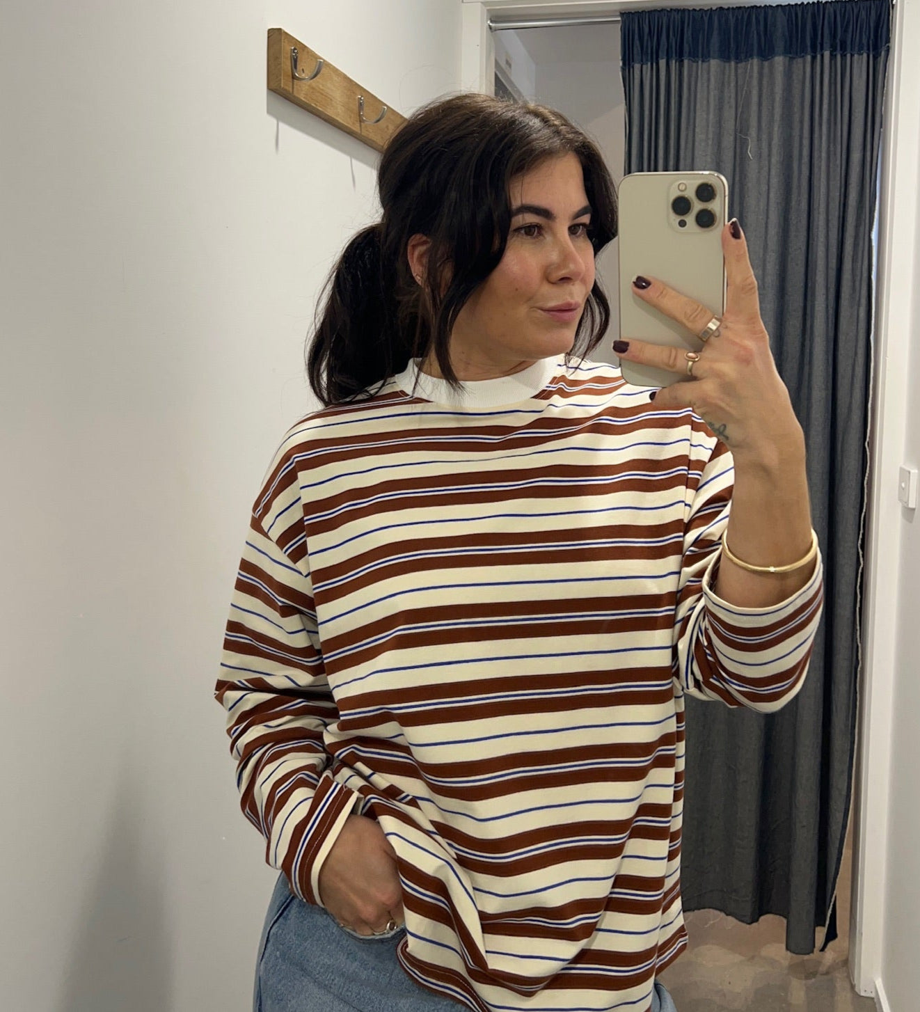 Person taking a mirror selfie wearing a striped sweater and jeans in a room.