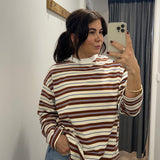 Person taking a mirror selfie wearing a striped sweater and jeans in a room.