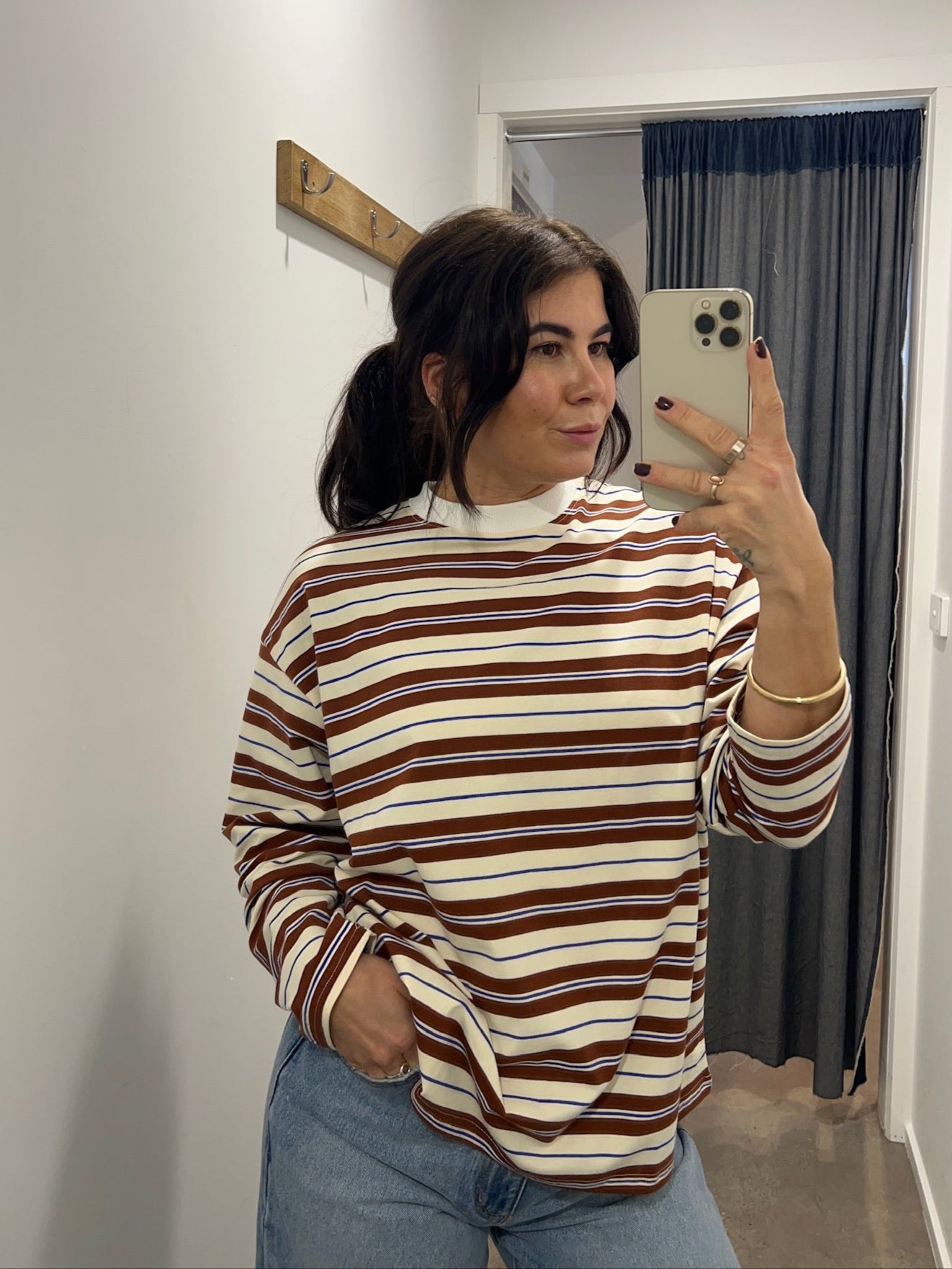 Person taking a mirror selfie wearing a striped sweater and jeans in a room.