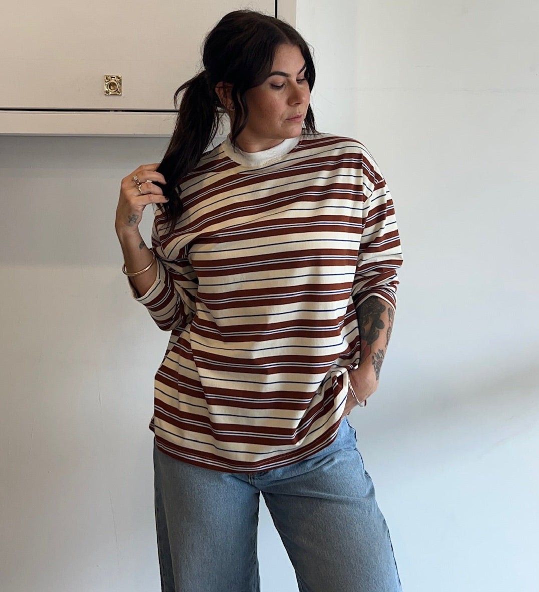 Woman wearing a striped sweater and jeans standing against a white wall.