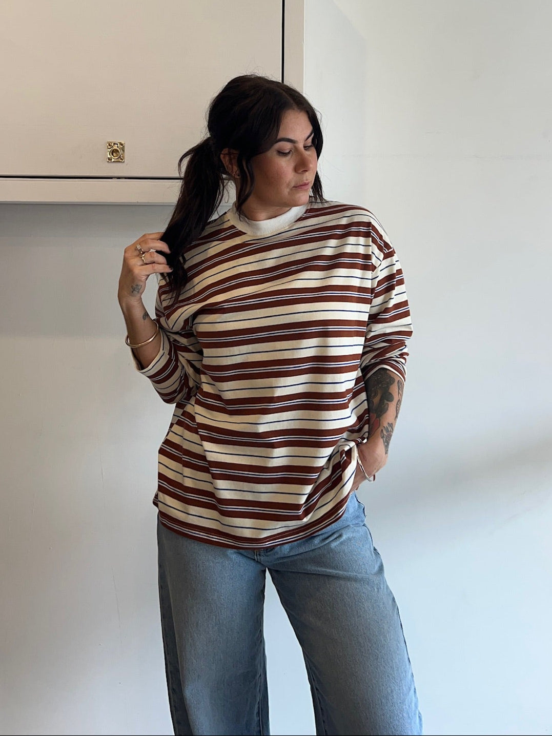Woman wearing a striped sweater and jeans standing against a white wall.