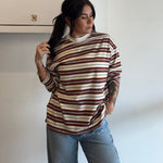 Woman wearing a striped sweater and jeans standing against a white wall.