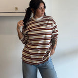 Woman wearing a striped sweater and jeans standing against a white wall.