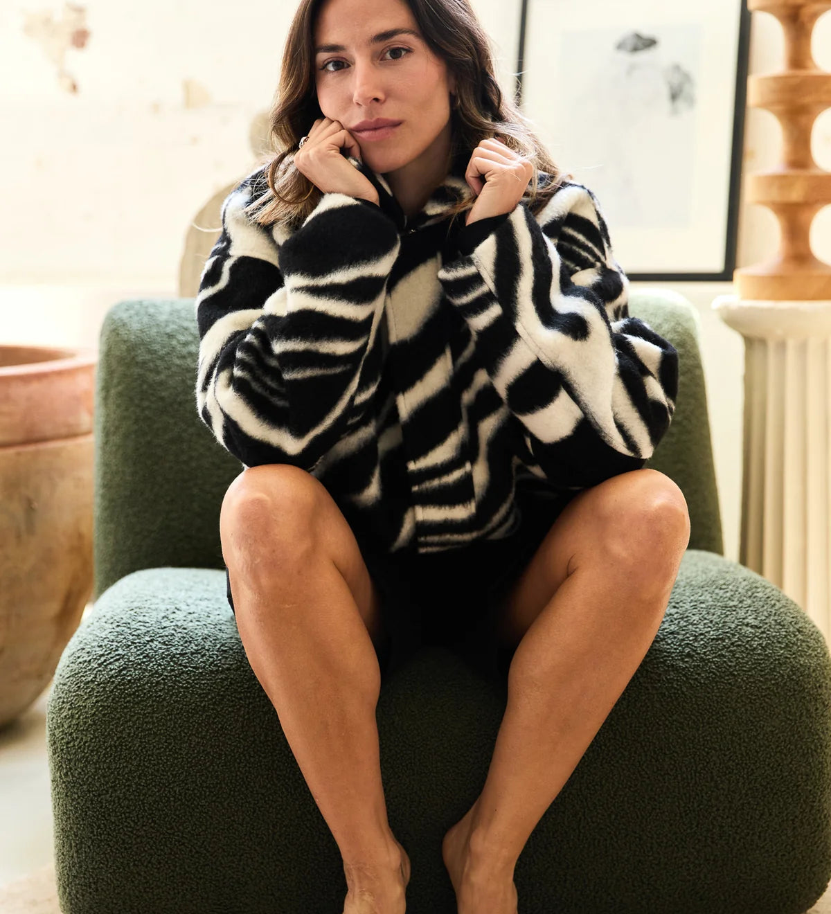 Woman sitting on a green chair wearing a zebra print sweater in a cozy room.