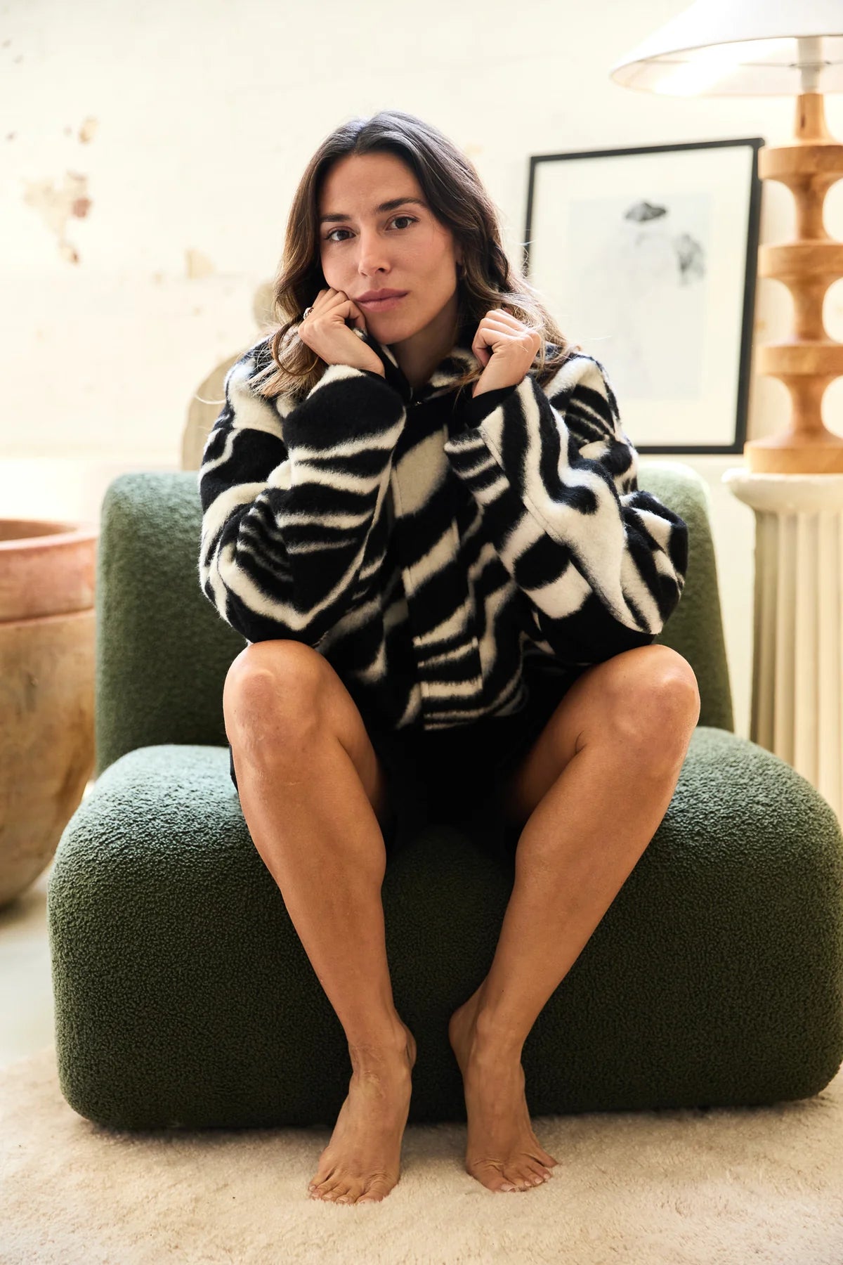 Woman sitting on a green chair wearing a zebra print sweater in a cozy room.