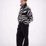 Person wearing a black and white patterned sweater with black pants on a white background
