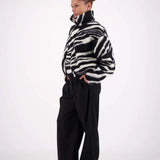 Person wearing a black and white patterned sweater with black pants on a white background