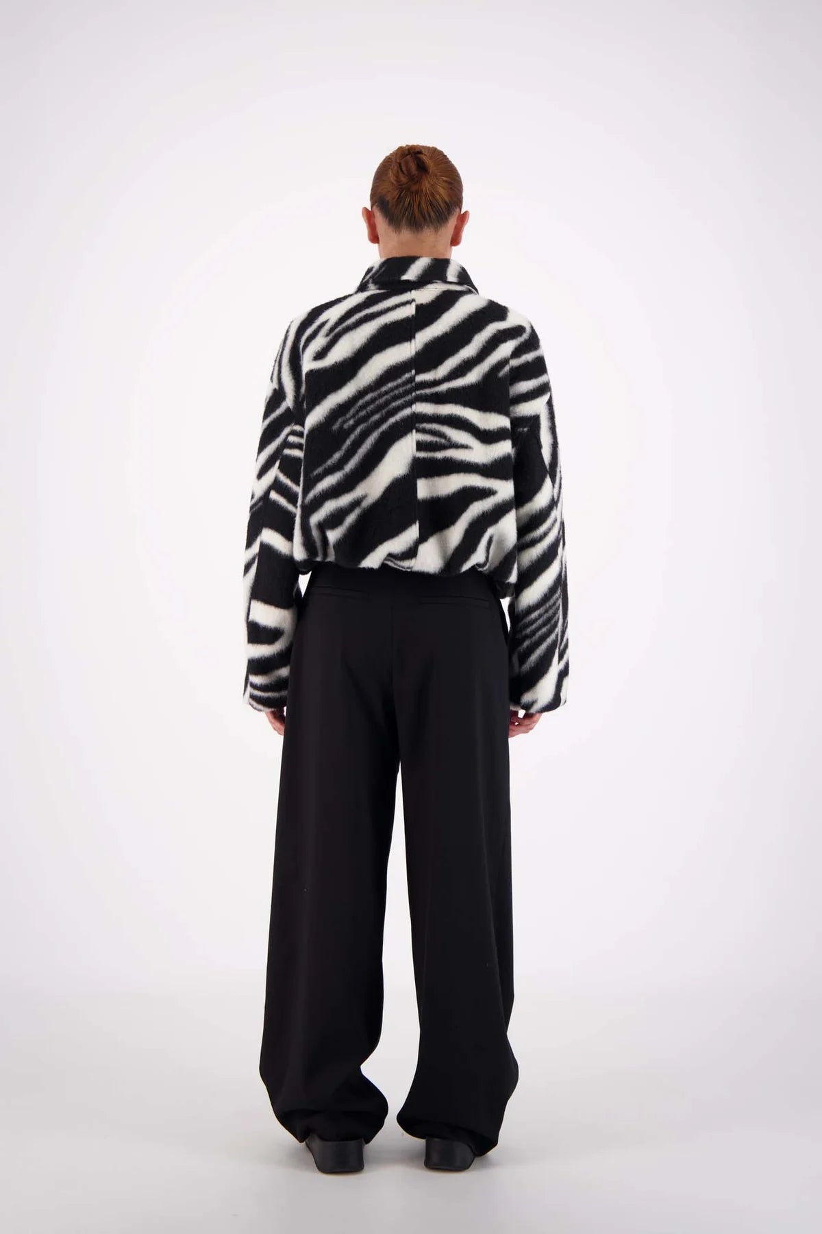 Person wearing a zebra-striped shirt and black pants on a white background