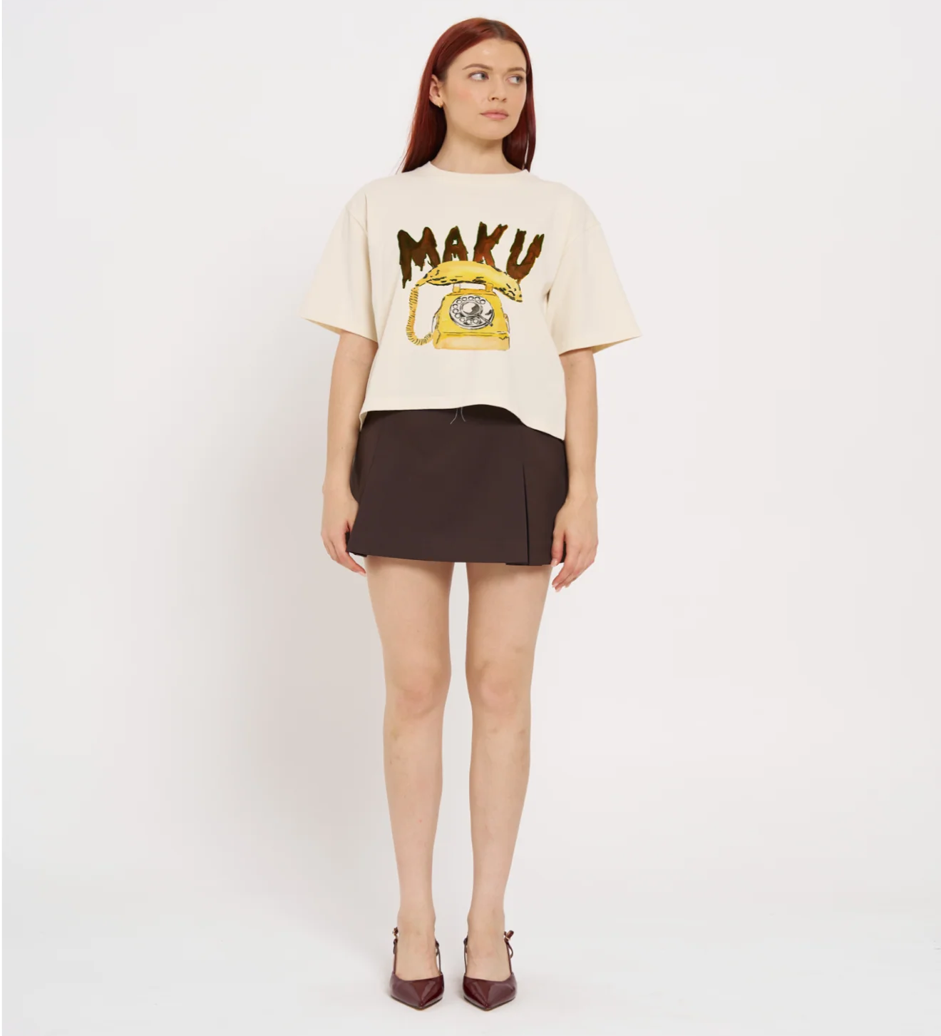 Woman wearing a cream t-shirt with 'MAKU' print and a brown skirt on a white background