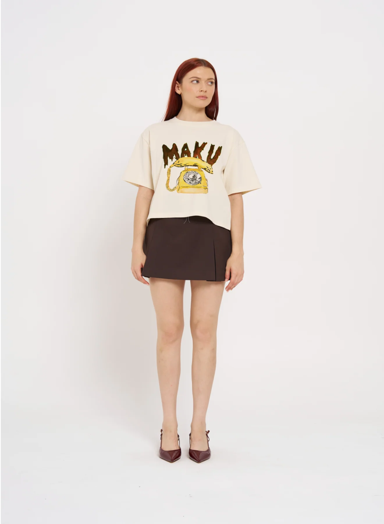 Woman wearing a cream t-shirt with 'MAKU' print and a brown skirt on a white background