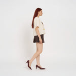 Woman wearing a cream t-shirt with 'MAKU' print and a brown skirt on a white background