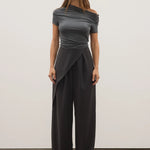 Woman wearing a gray off-shoulder top and black wide-leg pants against a white background