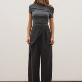 Woman wearing a gray off-shoulder top and black wide-leg pants against a white background