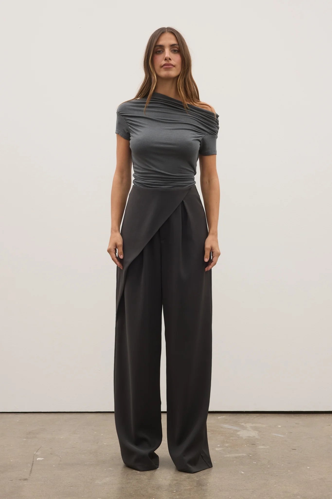 Woman wearing a gray off-shoulder top and black wide-leg pants against a white background