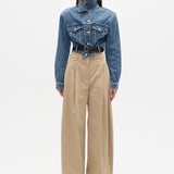 Person wearing a blue denim jacket and beige pants on a white background
