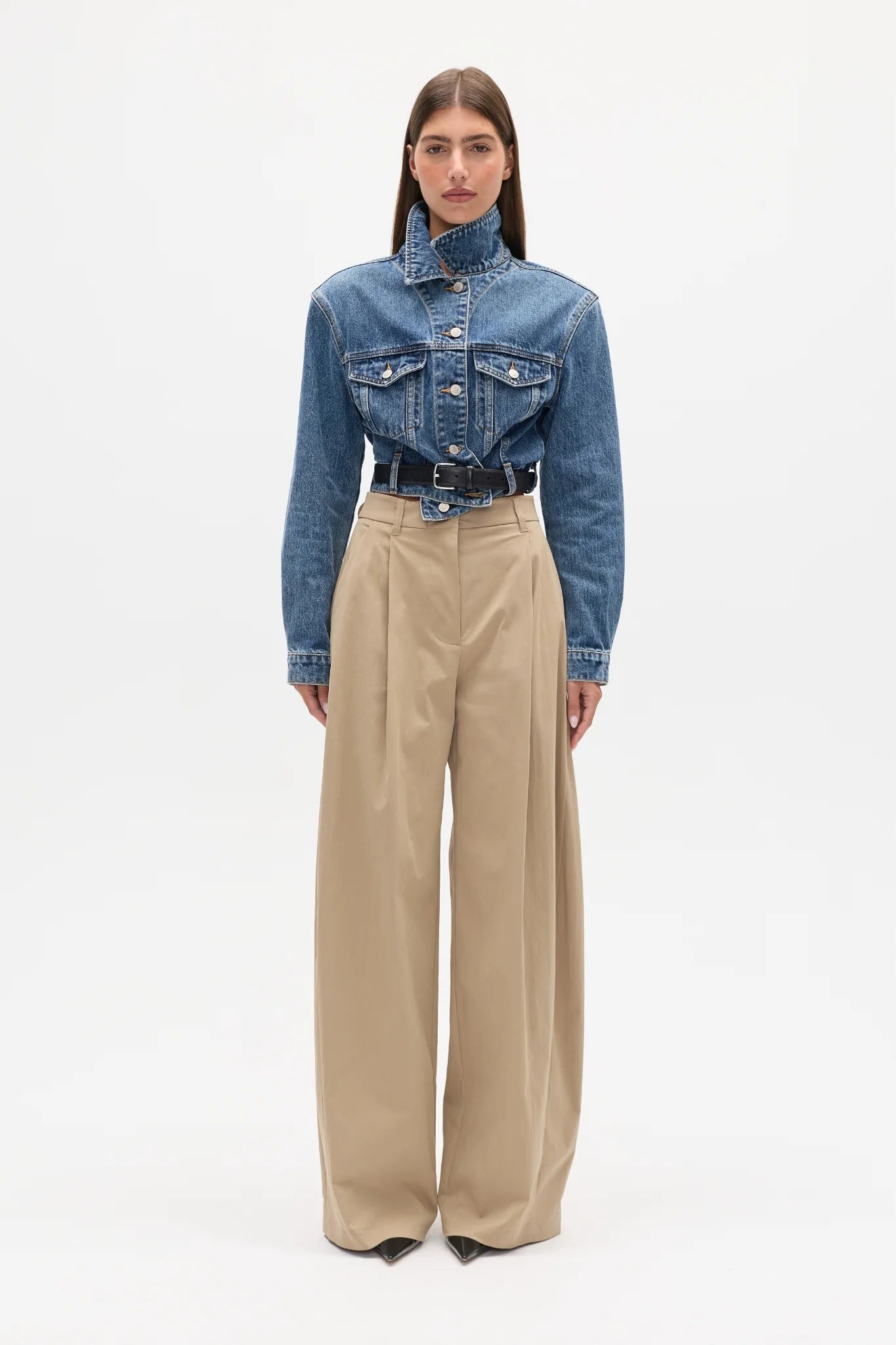 Person wearing a blue denim jacket and beige pants on a white background