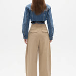 Person wearing a blue denim jacket and beige pants on a white background