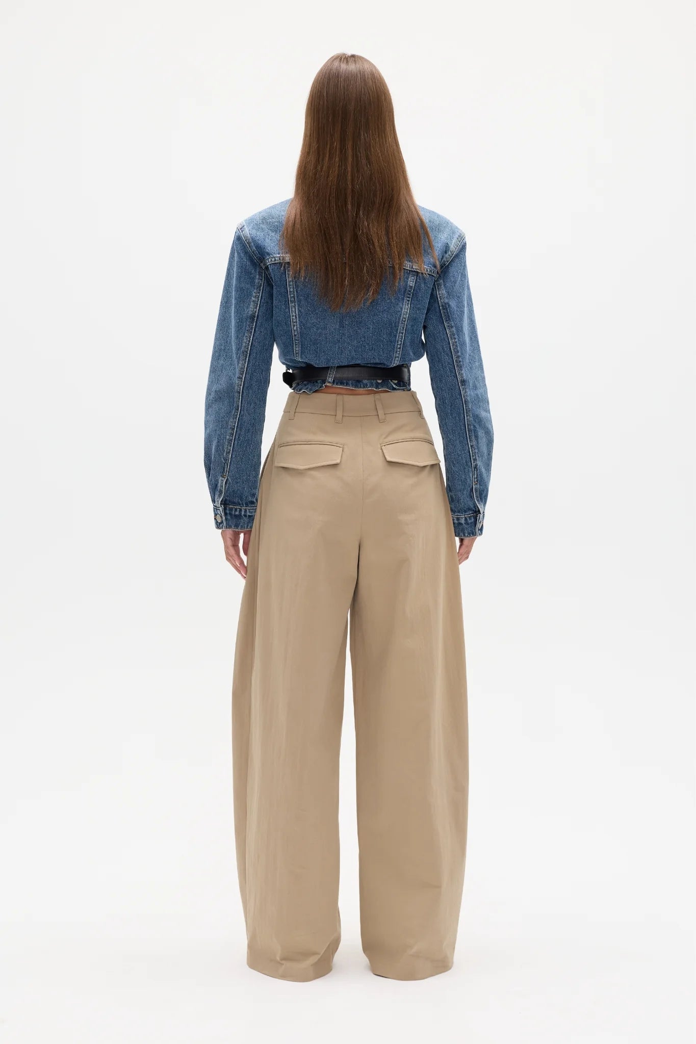 Person wearing a blue denim jacket and beige pants on a white background