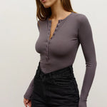 Woman wearing a long-sleeve purple top and black pants on a plain background