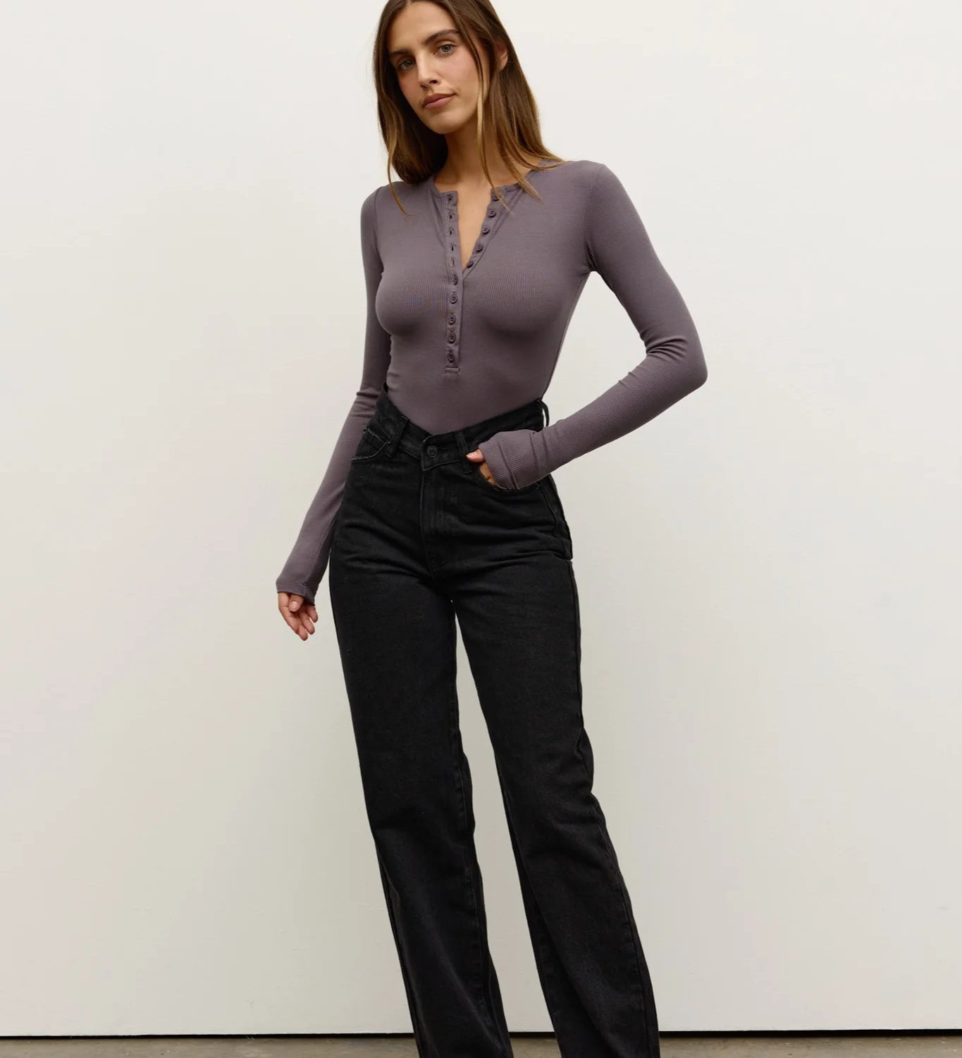 Woman wearing a purple long-sleeve top and black pants against a white background