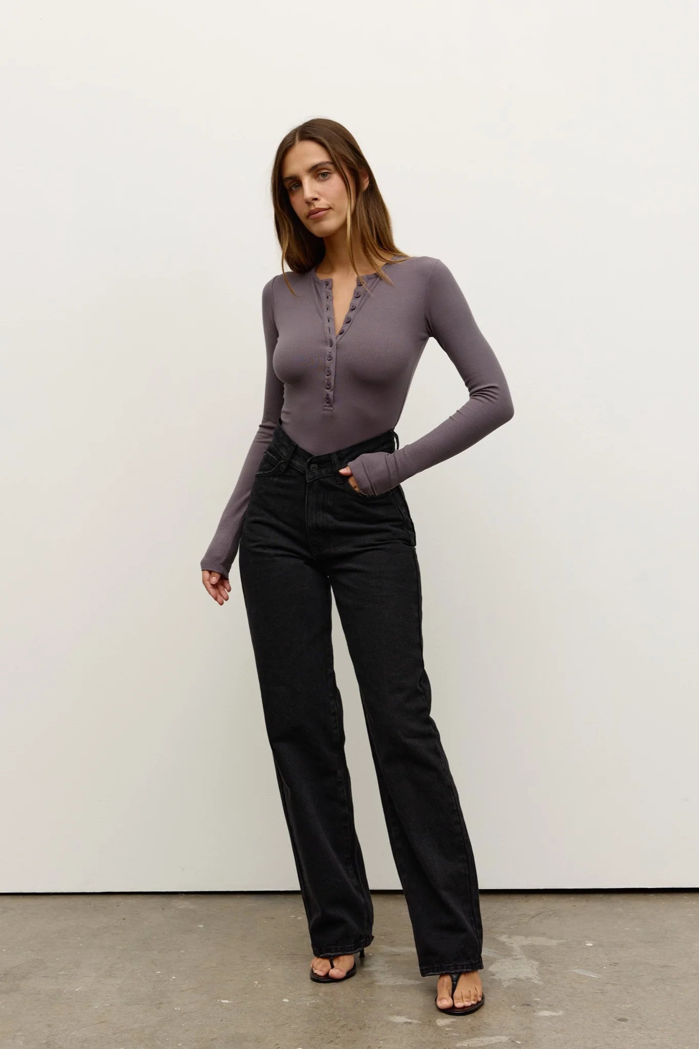 Woman wearing a purple long-sleeve top and black pants against a white background