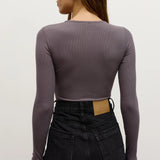 Woman wearing a long-sleeve purple top and black pants on a plain background